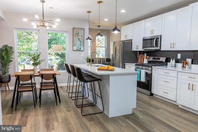 kitchen with pendant lighting, white cabinetry, stainless steel appliances, and a kitchen island with sink