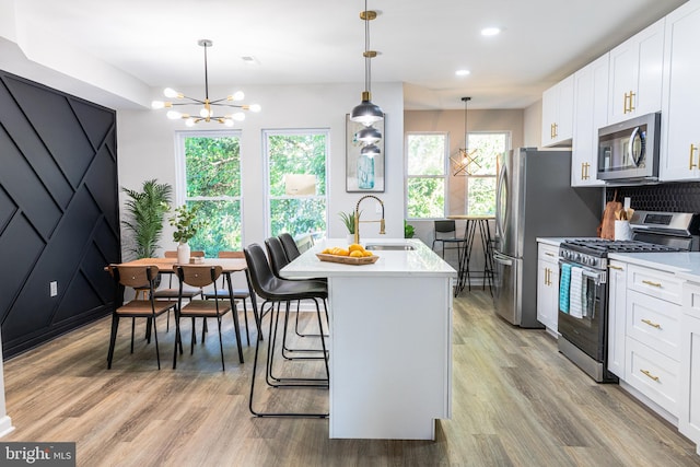 kitchen featuring white cabinetry, a wealth of natural light, hanging light fixtures, a kitchen island with sink, and appliances with stainless steel finishes