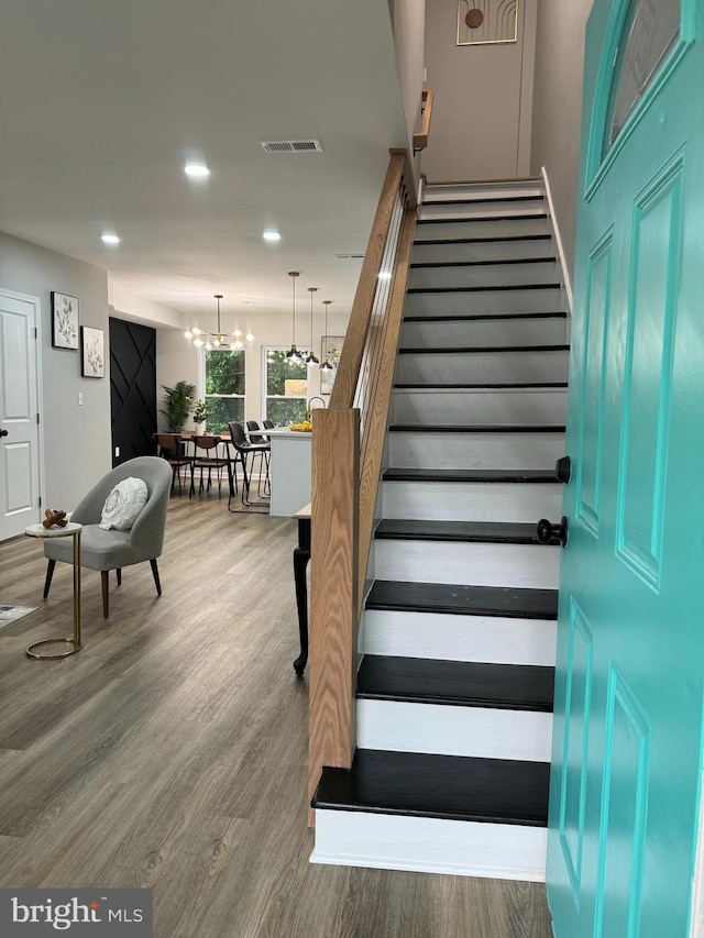 staircase with hardwood / wood-style floors and a chandelier