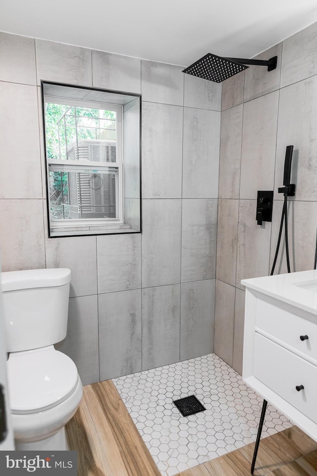 bathroom with toilet, vanity, tile walls, and tiled shower