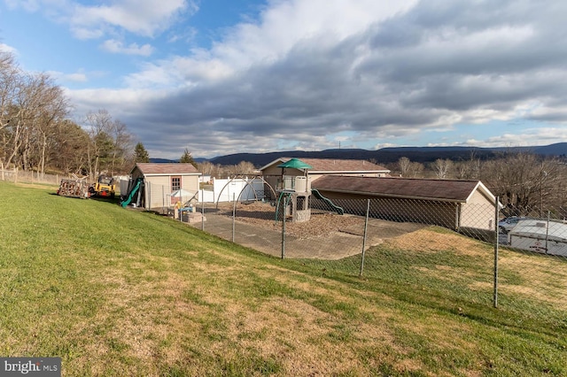 exterior space with a mountain view, a playground, a storage unit, and a lawn