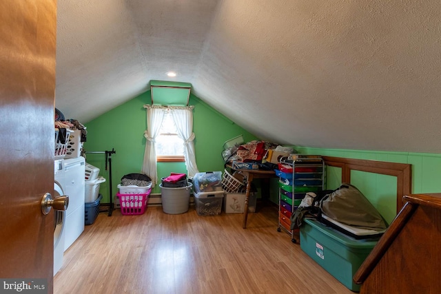 additional living space with vaulted ceiling, washing machine and dryer, a textured ceiling, and light hardwood / wood-style flooring