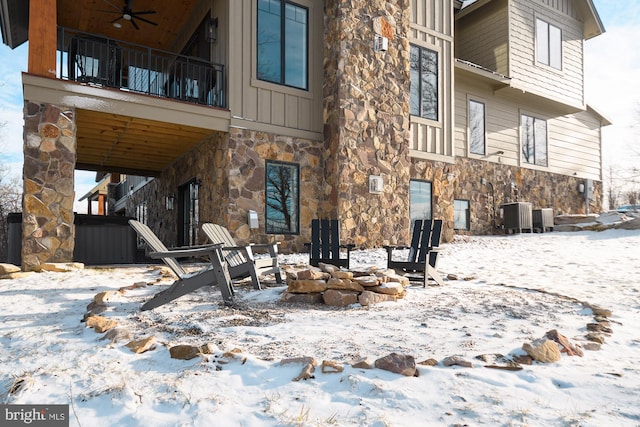 snow covered back of property with ceiling fan, a balcony, and central AC unit