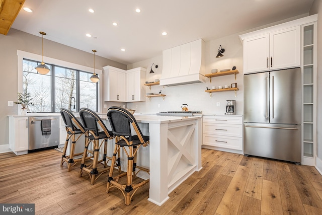 kitchen with stainless steel refrigerator, light hardwood / wood-style flooring, pendant lighting, white cabinets, and custom exhaust hood