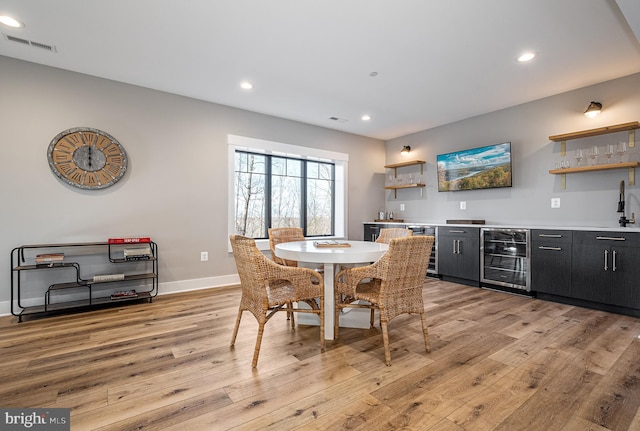 dining space featuring indoor wet bar, wine cooler, and light hardwood / wood-style flooring