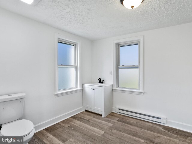 bathroom with a healthy amount of sunlight, hardwood / wood-style floors, a baseboard radiator, and toilet