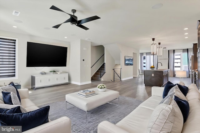 living room with sink, light hardwood / wood-style floors, and ceiling fan with notable chandelier