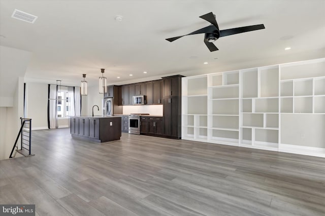 kitchen featuring hardwood / wood-style floors, stainless steel appliances, dark brown cabinets, and a center island with sink