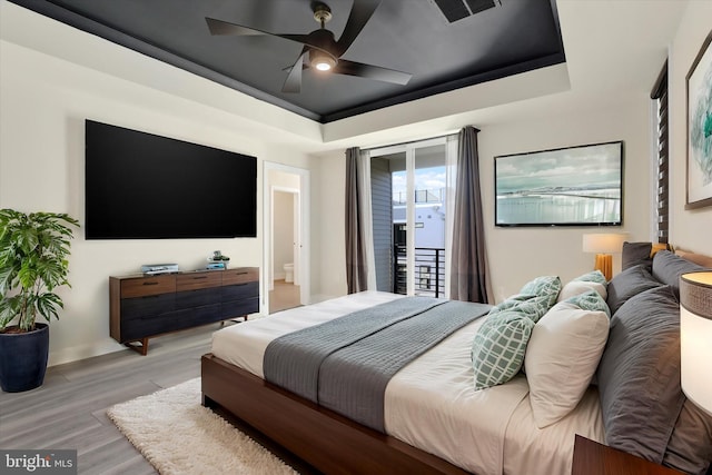 bedroom featuring ceiling fan, light hardwood / wood-style floors, access to outside, and a tray ceiling