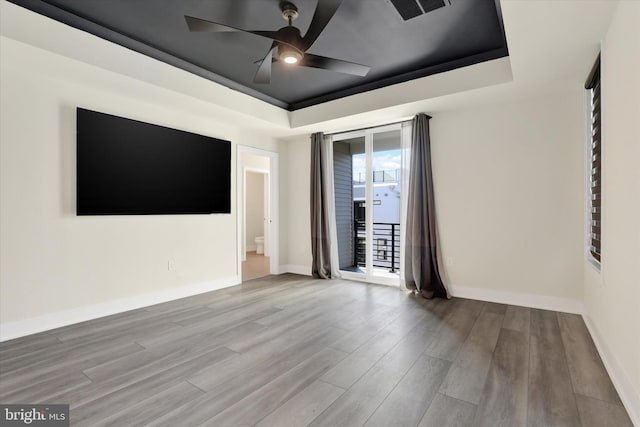 spare room with light wood-type flooring, a tray ceiling, and ceiling fan