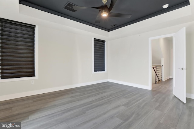 spare room featuring a tray ceiling, ceiling fan, and light hardwood / wood-style flooring