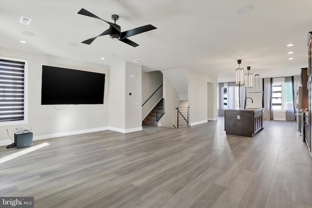 unfurnished living room featuring ceiling fan with notable chandelier, light hardwood / wood-style flooring, and sink