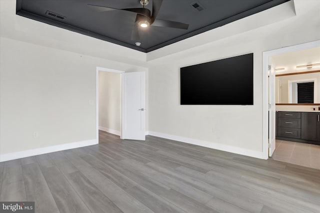 empty room featuring ceiling fan, light hardwood / wood-style floors, and a tray ceiling