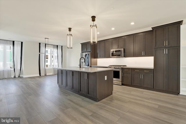 kitchen featuring appliances with stainless steel finishes, light wood-type flooring, dark brown cabinetry, pendant lighting, and a center island with sink