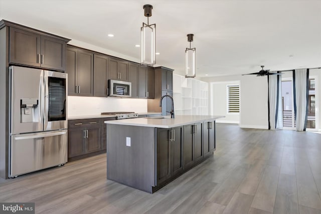 kitchen featuring a kitchen island with sink, sink, decorative light fixtures, light hardwood / wood-style floors, and stainless steel appliances