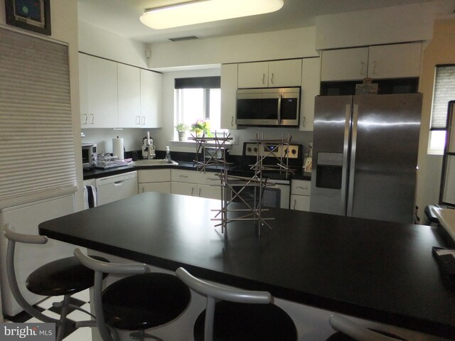1710 Oakwood Ter Unit 3E, Penn Valley, PA 19072 - kitchen with appliances with stainless steel finishes, dark countertops, white cabinetry, a kitchen breakfast bar, and a sink
