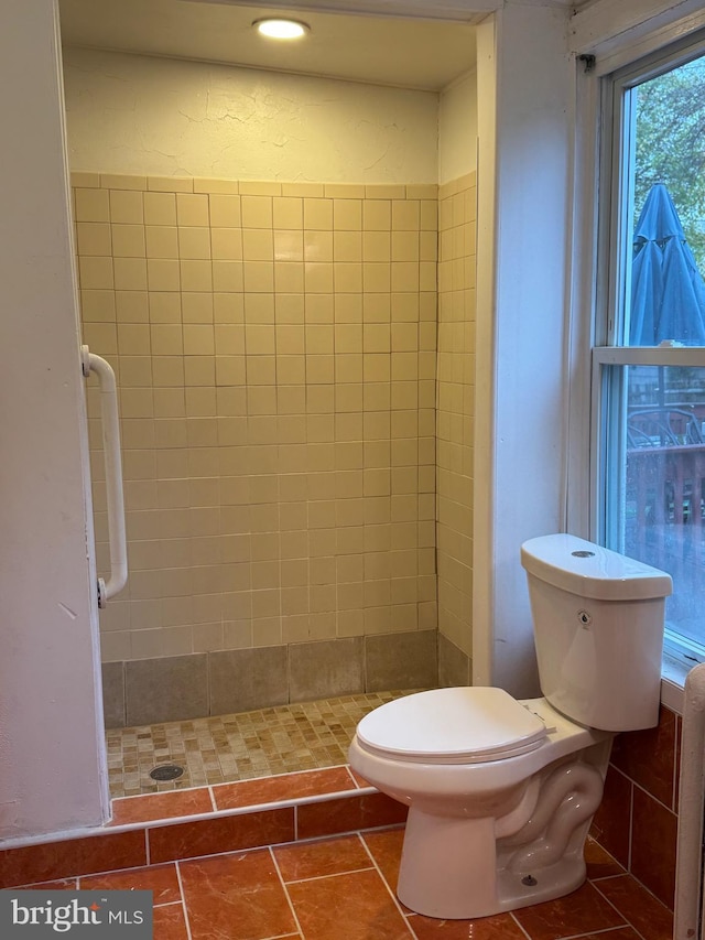 bathroom with tile patterned flooring, toilet, and a tile shower