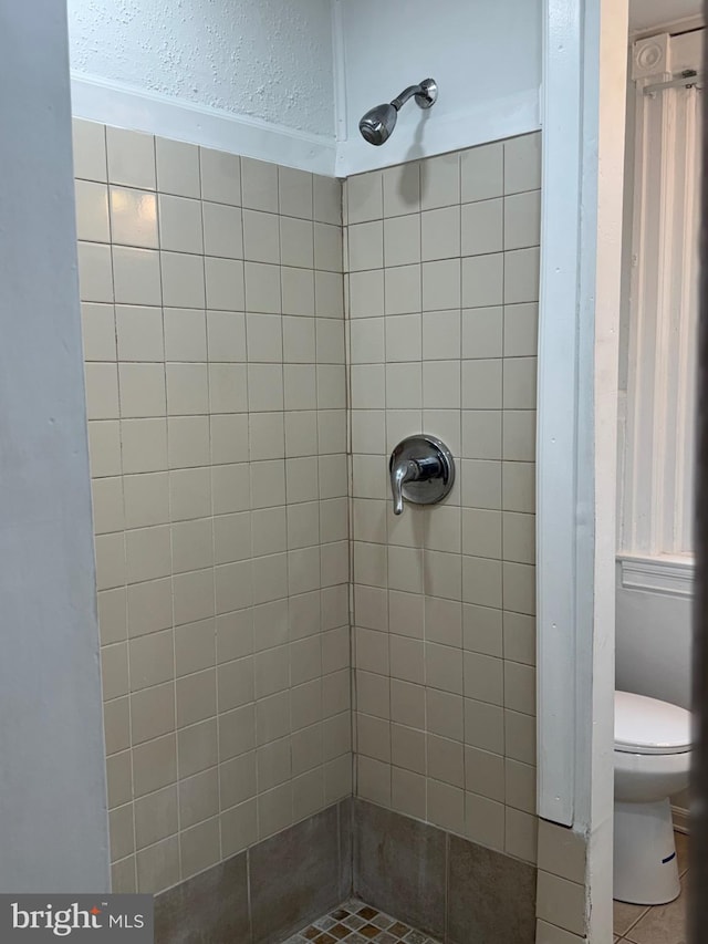 bathroom featuring tile patterned floors, toilet, and a tile shower