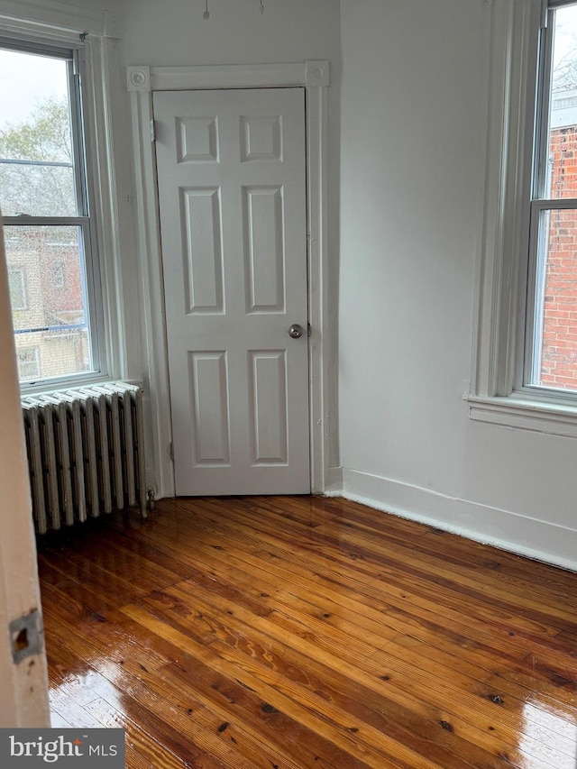 spare room featuring radiator heating unit, a healthy amount of sunlight, and wood-type flooring