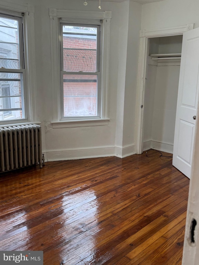 unfurnished bedroom featuring radiator heating unit, dark hardwood / wood-style flooring, and a closet