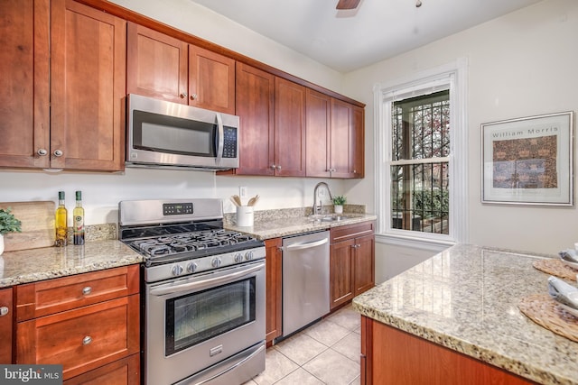 kitchen with sink, ceiling fan, light stone countertops, light tile patterned floors, and stainless steel appliances