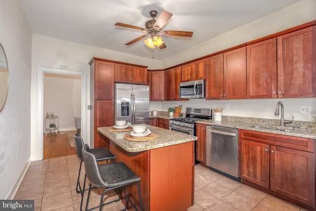 kitchen featuring light stone countertops, a center island, stainless steel appliances, and sink