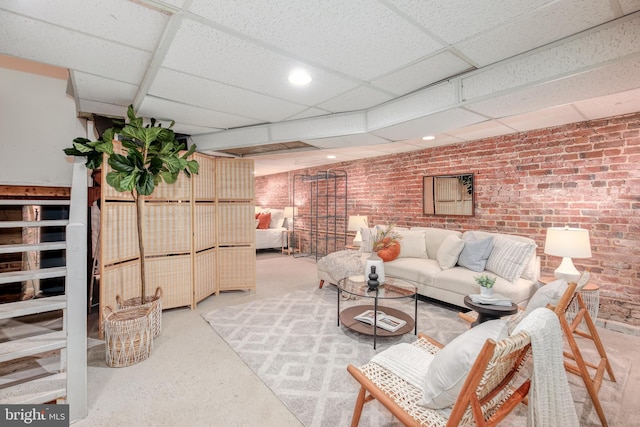 living room featuring a drop ceiling and brick wall