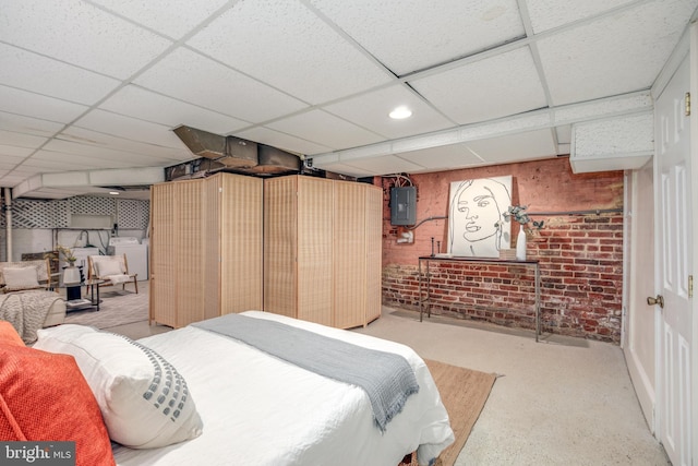 bedroom with electric panel, a drop ceiling, brick wall, and washer / dryer