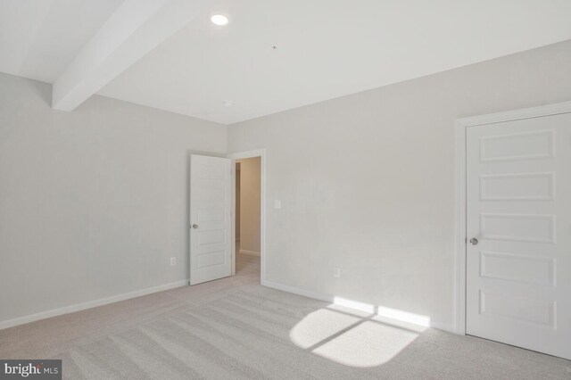 empty room with beamed ceiling and light colored carpet