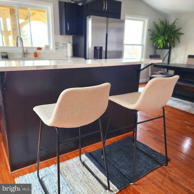 kitchen featuring stainless steel fridge, a kitchen breakfast bar, vaulted ceiling, blue cabinetry, and hardwood / wood-style floors