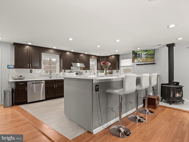 kitchen with a center island, a wood stove, light hardwood / wood-style floors, stainless steel dishwasher, and dark brown cabinets