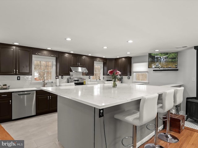 kitchen featuring stainless steel appliances, sink, light stone counters, a breakfast bar area, and a kitchen island