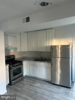 kitchen with light hardwood / wood-style floors, white cabinetry, stainless steel appliances, and extractor fan