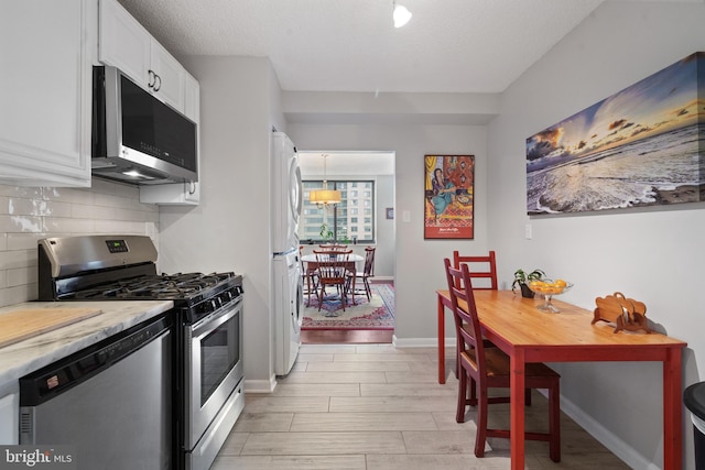 3701 S George Mason Dr Unit 1005N, Falls Church, VA 22041 - kitchen featuring stainless steel appliances, white cabinetry, decorative backsplash, wood tiled floor, and stacked washer and clothes dryer
