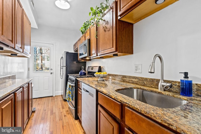 kitchen featuring stainless steel appliances, sink, dark stone countertops, and light hardwood / wood-style floors