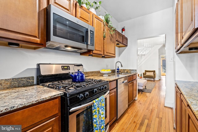 kitchen featuring stainless steel appliances, sink, stone counters, and light wood-type flooring