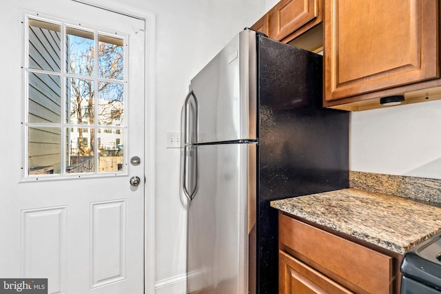 kitchen featuring electric range oven, light stone countertops, and stainless steel refrigerator