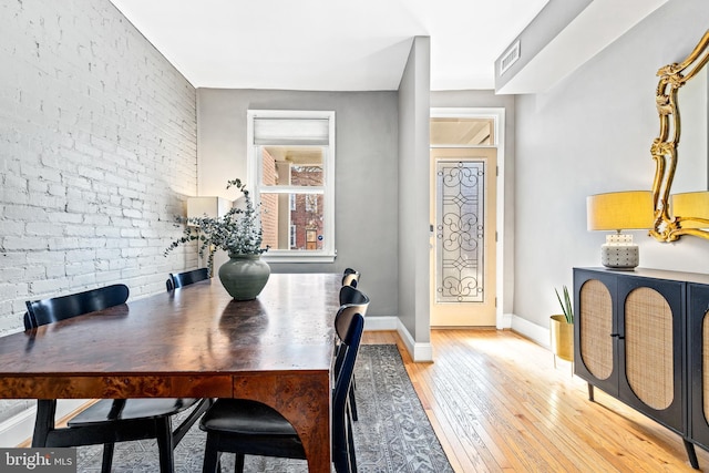 dining room featuring brick wall and light hardwood / wood-style floors