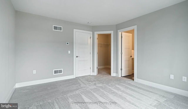 unfurnished bedroom featuring a walk in closet, light carpet, a closet, and ensuite bath