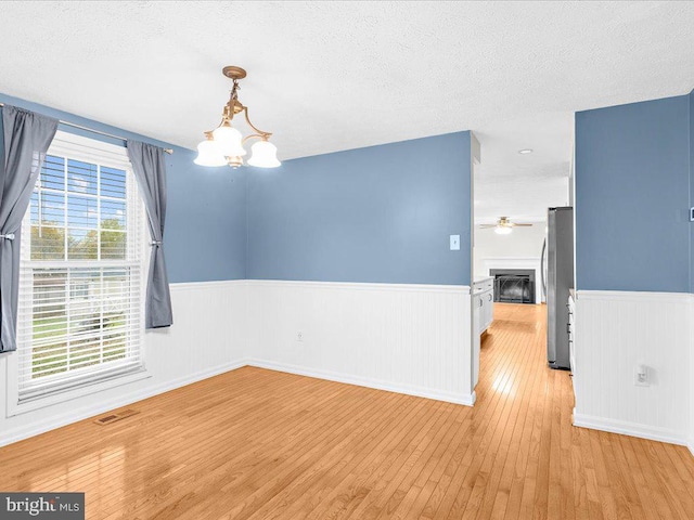 spare room with ceiling fan with notable chandelier, light hardwood / wood-style floors, and a textured ceiling