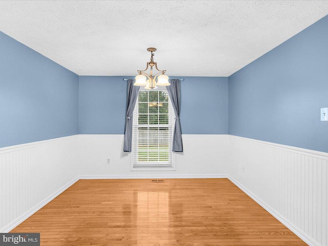 spare room featuring wood-type flooring, a textured ceiling, and a notable chandelier