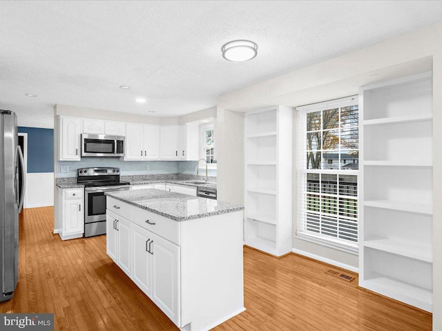 kitchen featuring light stone counters, a textured ceiling, stainless steel appliances, light hardwood / wood-style flooring, and white cabinets