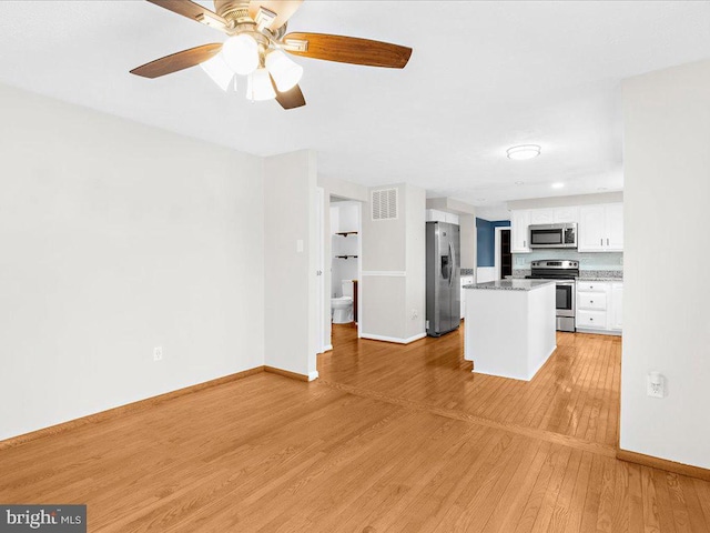 kitchen featuring white cabinets, light hardwood / wood-style flooring, ceiling fan, dark stone countertops, and appliances with stainless steel finishes