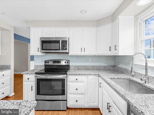 kitchen with white cabinets, light wood-type flooring, stainless steel appliances, and sink