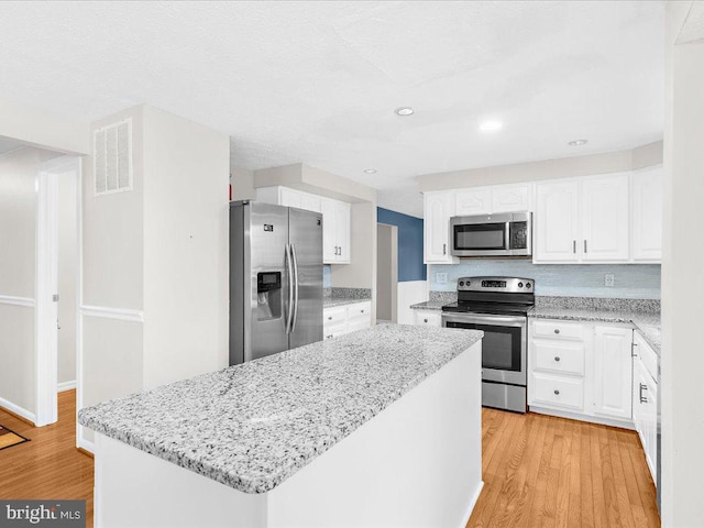 kitchen with white cabinets, a center island, light hardwood / wood-style floors, and stainless steel appliances