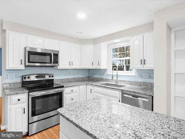 kitchen with backsplash, white cabinets, sink, light hardwood / wood-style floors, and stainless steel appliances