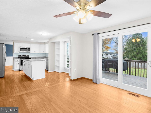 kitchen with light wood-type flooring, light stone counters, stainless steel appliances, ceiling fan, and white cabinets