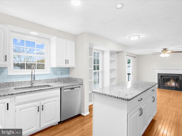 kitchen featuring sink, stainless steel dishwasher, decorative backsplash, light wood-type flooring, and white cabinetry