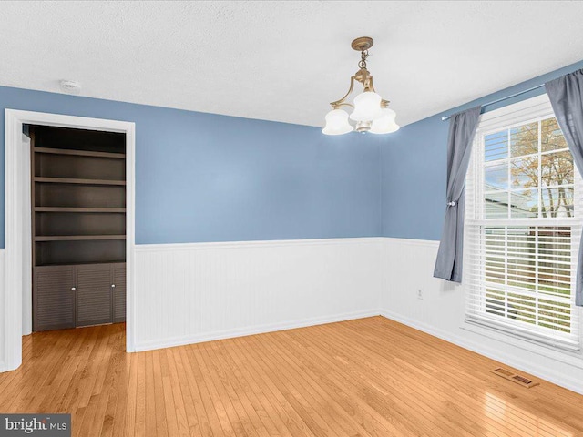 empty room featuring hardwood / wood-style floors, a textured ceiling, an inviting chandelier, and built in shelves