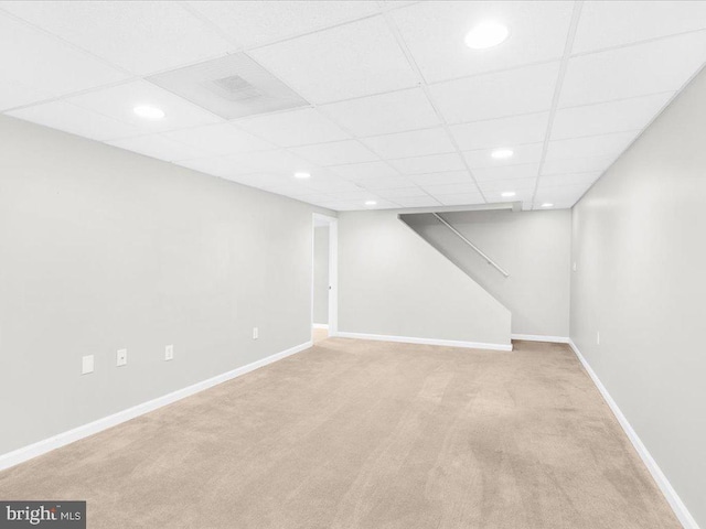 basement with a drop ceiling and light carpet